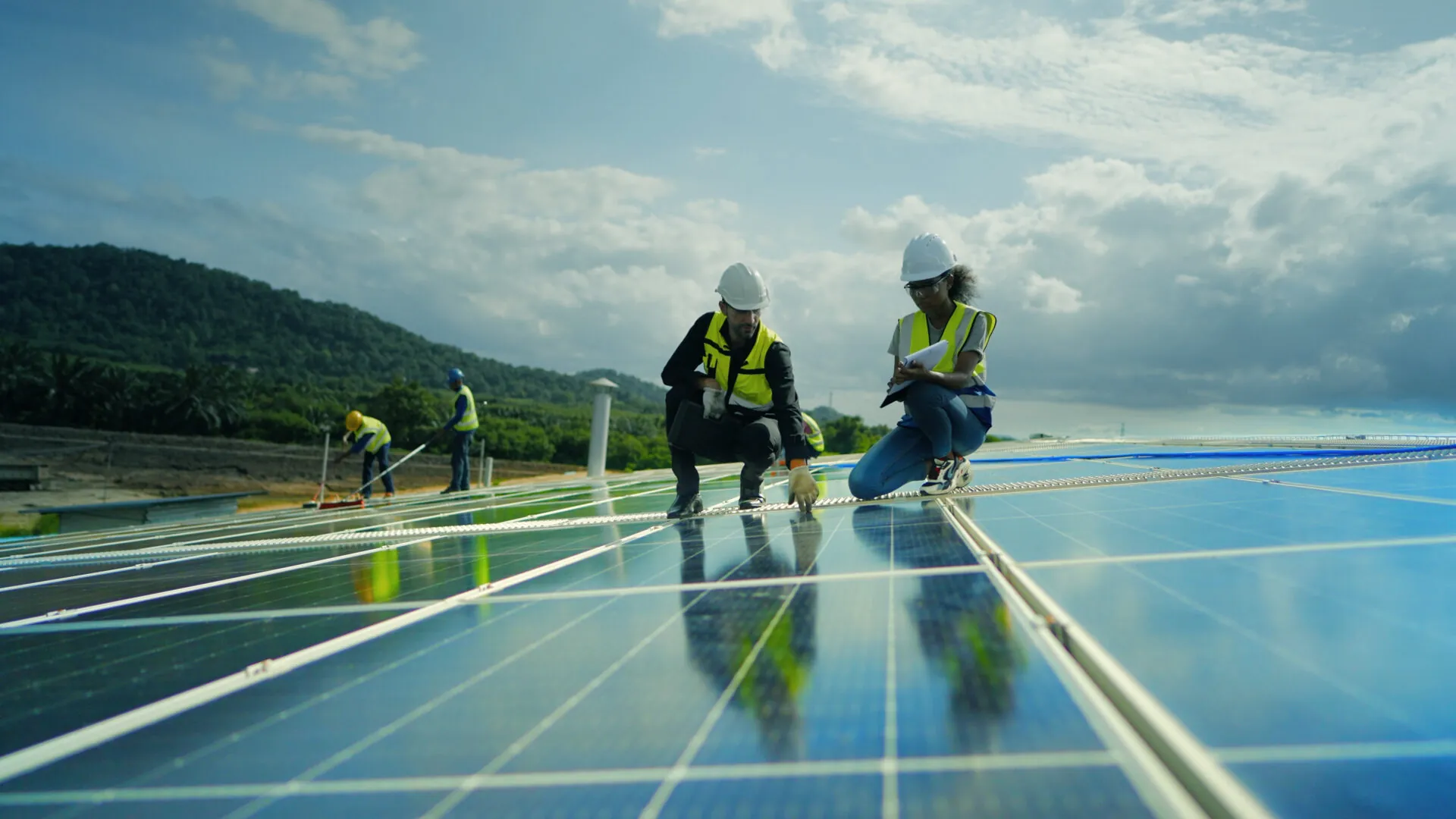 Team contractor, male engineer and female technicians wearing safety uniform, talking about installing plan, check the working system and maintenance solar panel of solar power plant to produce electricity on the roof of factory building.